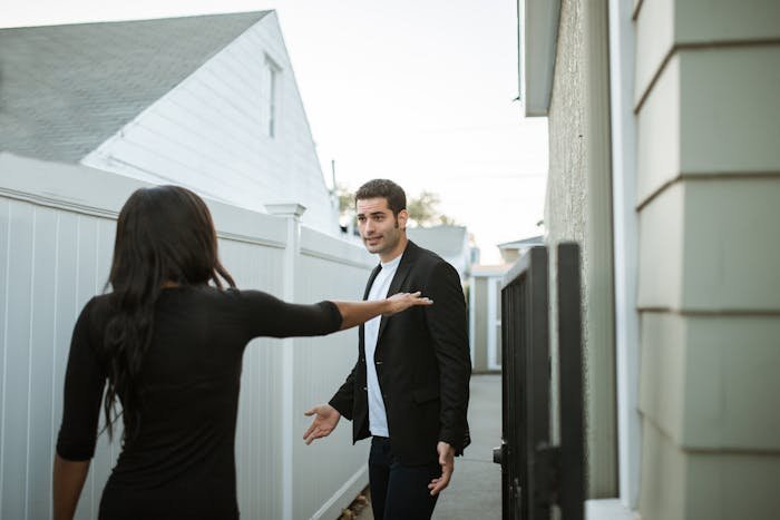 Woman and man arguing near fences, illustrating neighbors try to force woman to trim living hedge dividing properties.