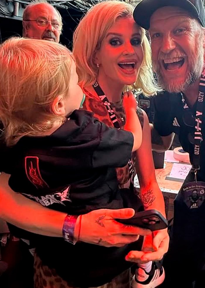 Kelly Osbourne smiling and holding a child, with fans around her, an odd detail sparks fan concern for doctor visit.