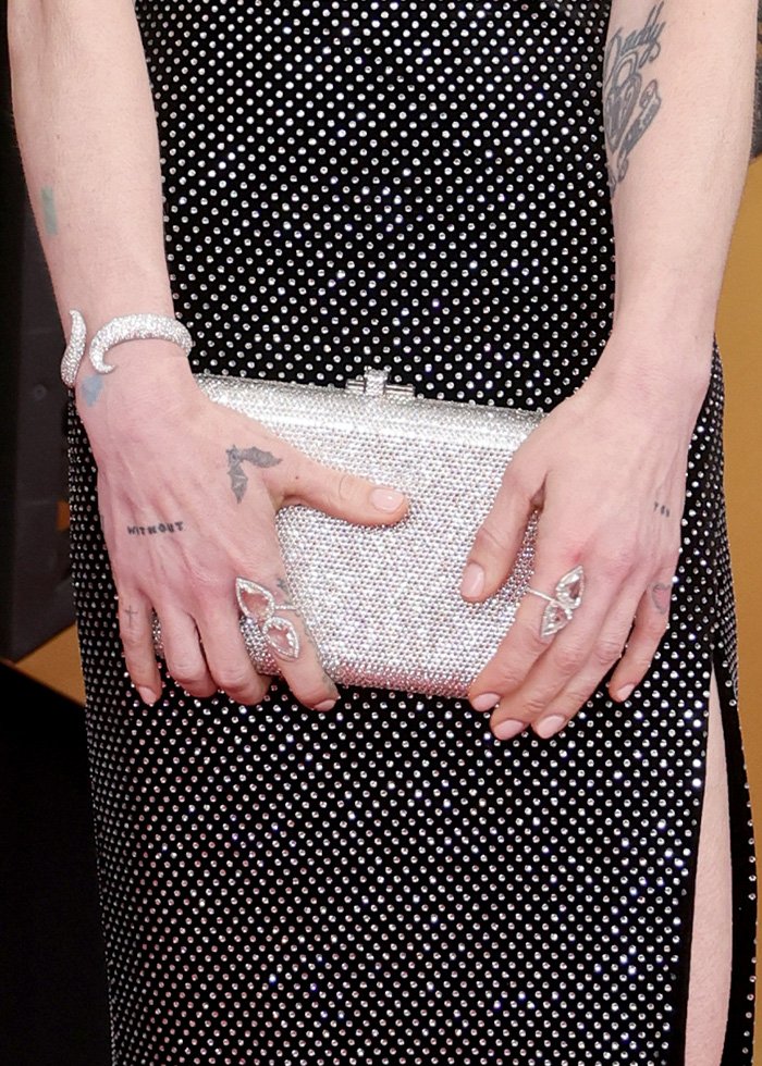 Close-up of hands with rings and tattoos holding a sparkling clutch, highlighting odd detail sparking fan concern about health.