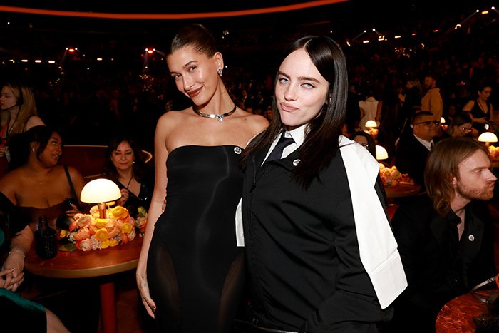 Two women posing at the Grammy event with other attendees in the background, highlighting Grammy seatfiller rules.
