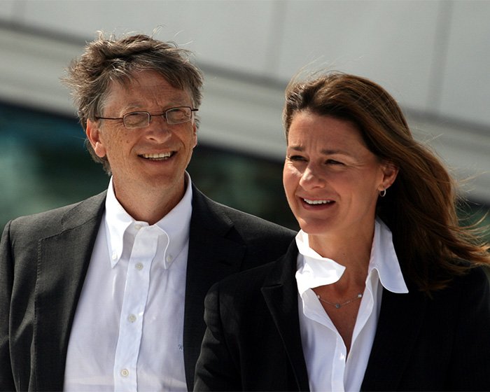 Bill Gates and Melinda French Gates together outdoors, both smiling and dressed in formal business attire.