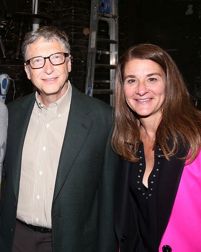 Melinda French Gates and Bill Gates smiling together indoors with dark background and casual attire.