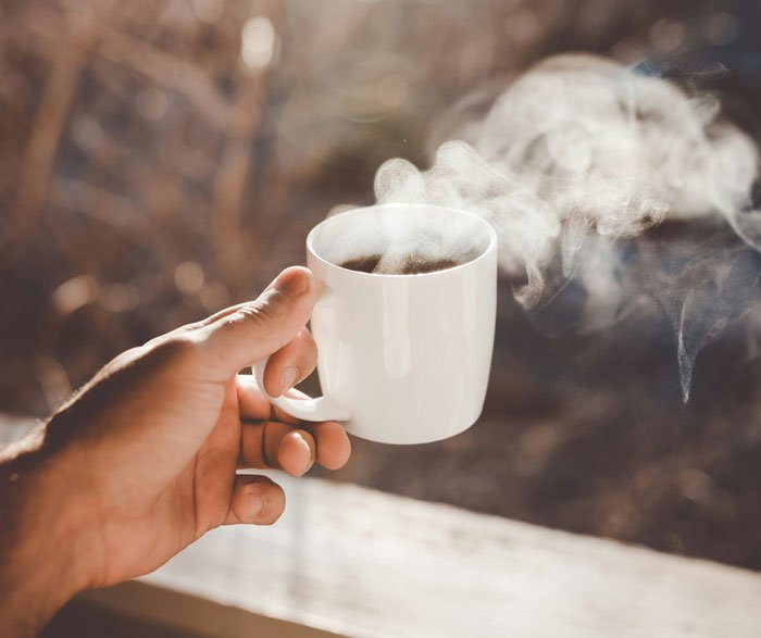 Hand holding a steaming white cup of coffee, illustrating a stunned woman reacting to roommate's parents using a spare key.