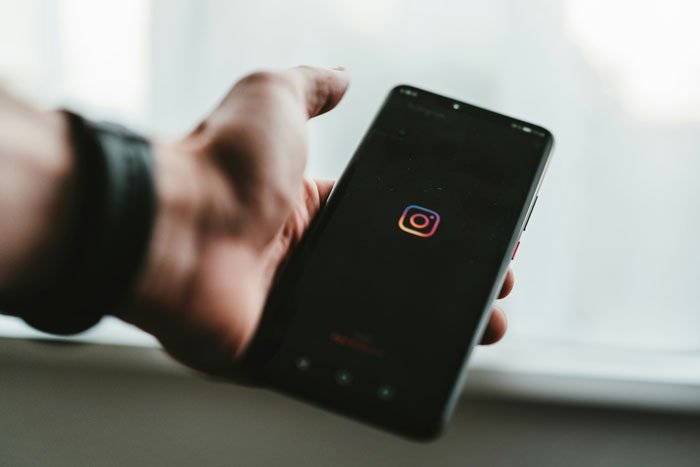 Hand holding smartphone displaying Instagram app, illustrating woman stunned by roommate&rsquo;s parents using spare key.