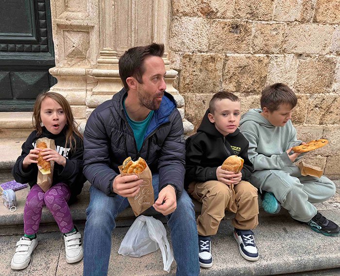 Father with four missing kids eating sandwiches on a stone step after their return from foreign orphanage abduction.