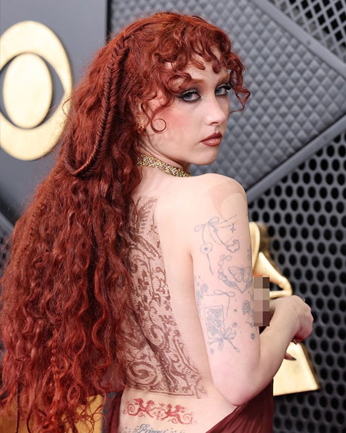 Person with long red curly hair and tattoos posing at an event, related to Grammy seat filler off-camera moments.