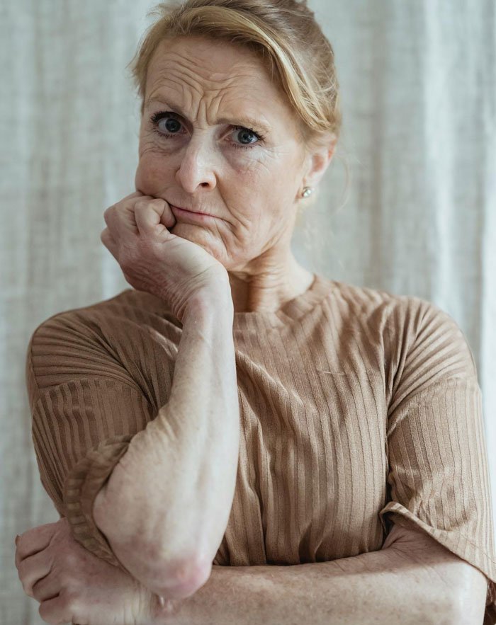 Concerned older woman with hand on chin, contemplating Mom's joke and the possibility of CPS involvement.