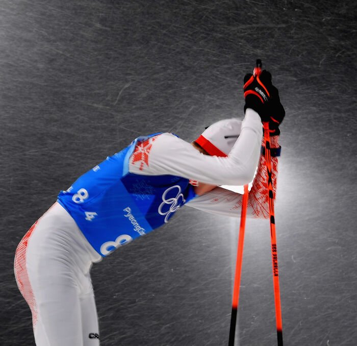 Cross-country skier in Winter Olympics gear leaning on poles amid snow, highlighting manhood scandal and rule change.