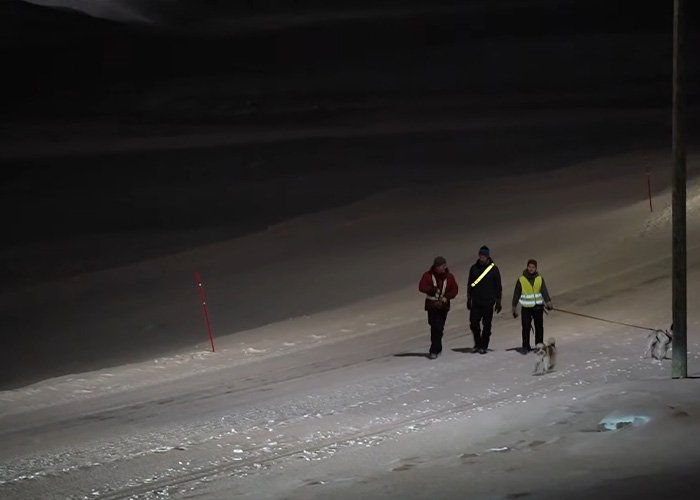 Three people with reflective gear walk dogs on a snow-covered road at night on the world’s darkest island.