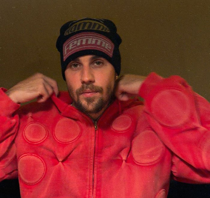 Justin Bieber wearing a red jacket and black beanie, linked to Epstein in disturbing theory by fans online.