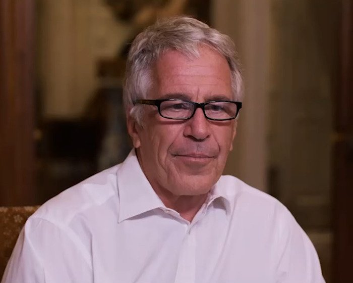 Older man with gray hair and black glasses wearing a white shirt in an indoor setting discussing viral theory claims Epstein.