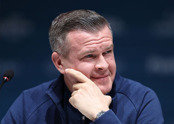 Man in a blue jacket at a press conference discussing Winter Olympics scandal involving skiers accused of cheating with acid use.