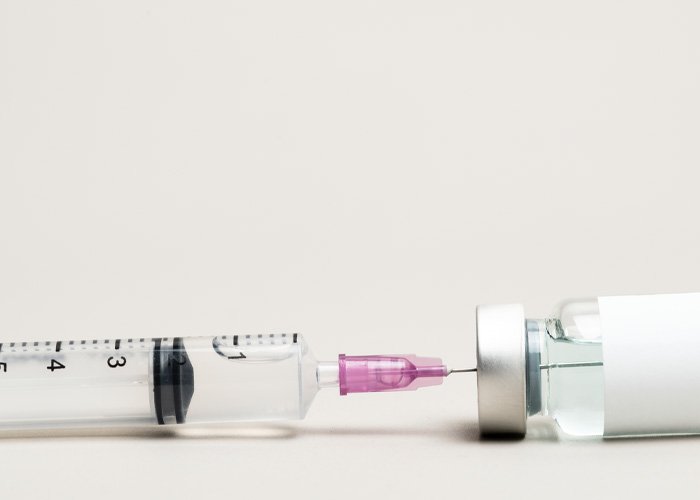 Syringe extracting clear hyaluronic acid solution from vial, illustrating injecting hyaluronic acid into manhood effects.