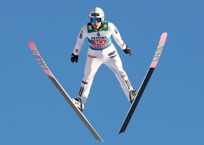 Ski jumper in mid-air against clear sky illustrating Olympic controversy amid hyaluronic acid injection debates.