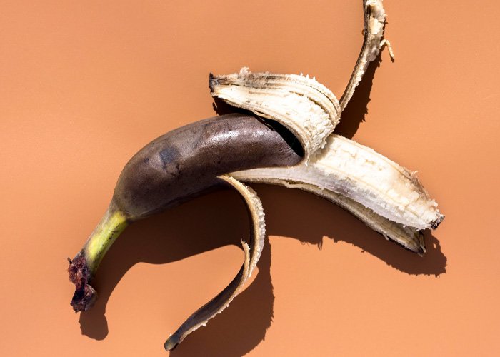 Partially peeled black banana on a plain background, symbolizing the effects of injecting hyaluronic acid into the manhood.