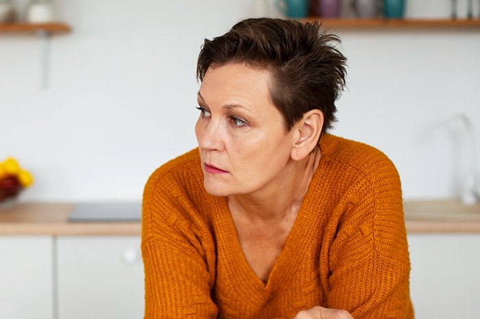 Woman in an orange sweater looking away pensively, illustrating emotional burden and cancer challenges.