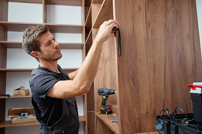 Man measuring wooden furniture while refusing free labor request in a home renovation setting.