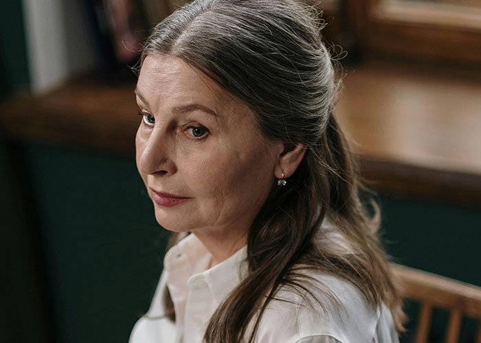 Older woman with gray hair looking sad indoors, capturing the tense mood between teen and stepmom on wedding day.