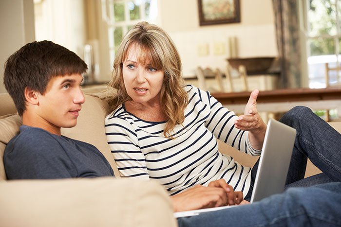 Teen looking frustrated while talking to his mom on a couch, illustrating teen sick of being a third parent at home.
