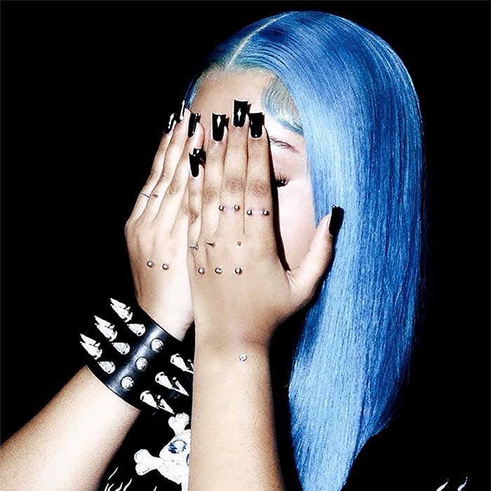 Person with blue hair, multiple hand piercings, and black nail polish covering face, highlighting recent piercing trends.