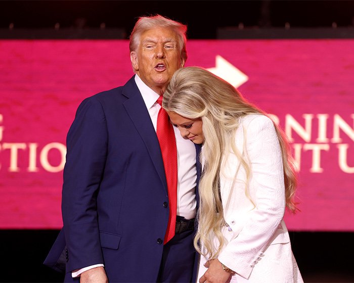 Man in a suit speaking closely with a woman in white at a Turning Point USA event, highlighting Erika Kirk controversy.