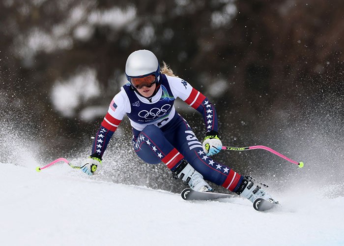 Lindsey Vonn skiing at Winter Olympics, wearing USA team suit, highlighting details behind ICU stay after crash.