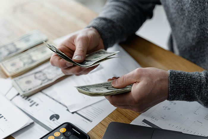 Hands counting US dollar bills over financial documents and calculator, illustrating girlfriend fixing finances alone.