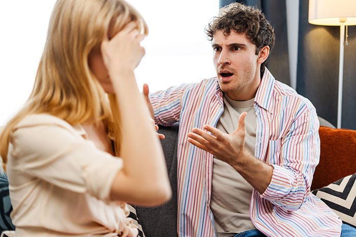 Young man giving girlfriend up to a year to fix finances, having serious discussion on a couch at home.