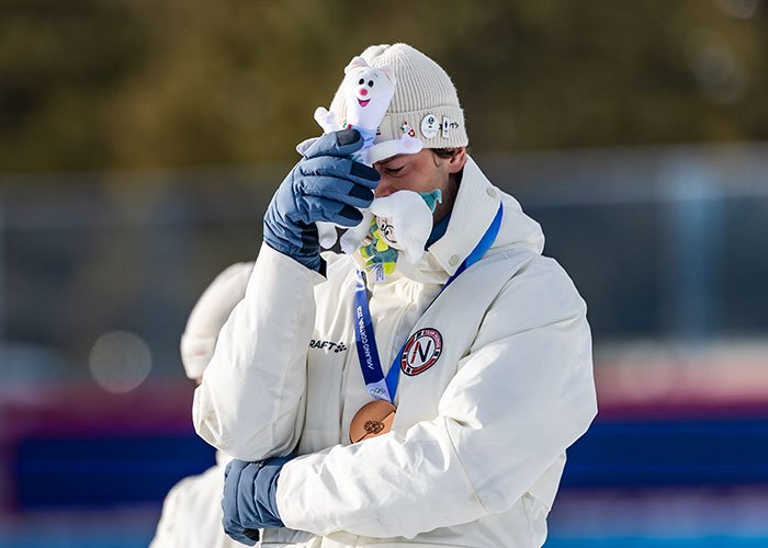 Olympic medalist in winter gear holding mascots, wearing bronze medal, showing emotion after medal victory.