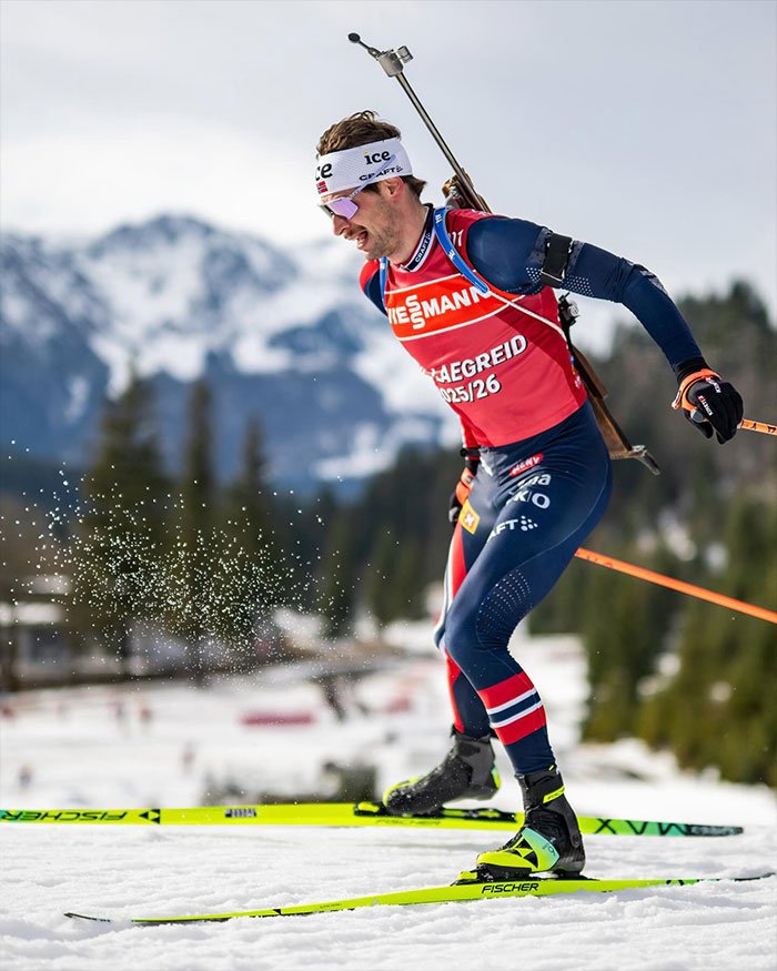 Olympic medalist skiing in winter sports gear with rifle on back during biathlon race in snowy mountain setting