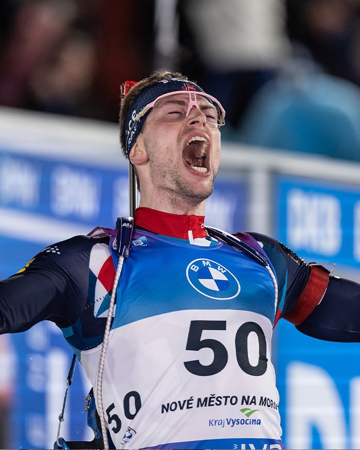 Olympic medalist celebrating with arms raised, wearing race bib 50 and sports gear during biathlon event.