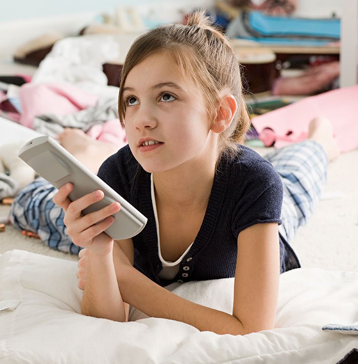 Young girl holding remote control lying on floor, symbolizing man’s marriage on the rocks after learning he has a 12YO daughter.