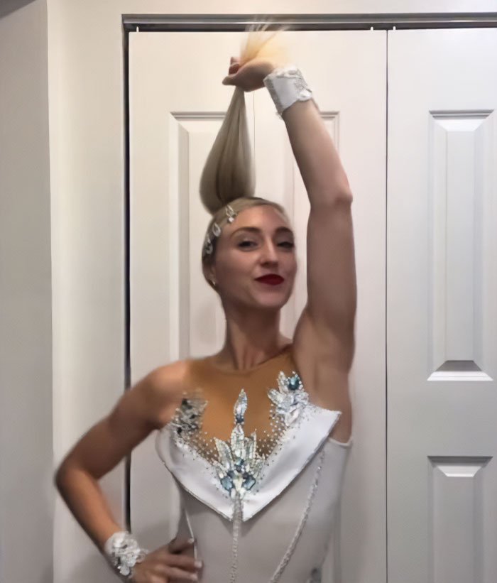 Olympic ice skater in a decorated costume holding hair up confidently after wardrobe malfunction during routine.