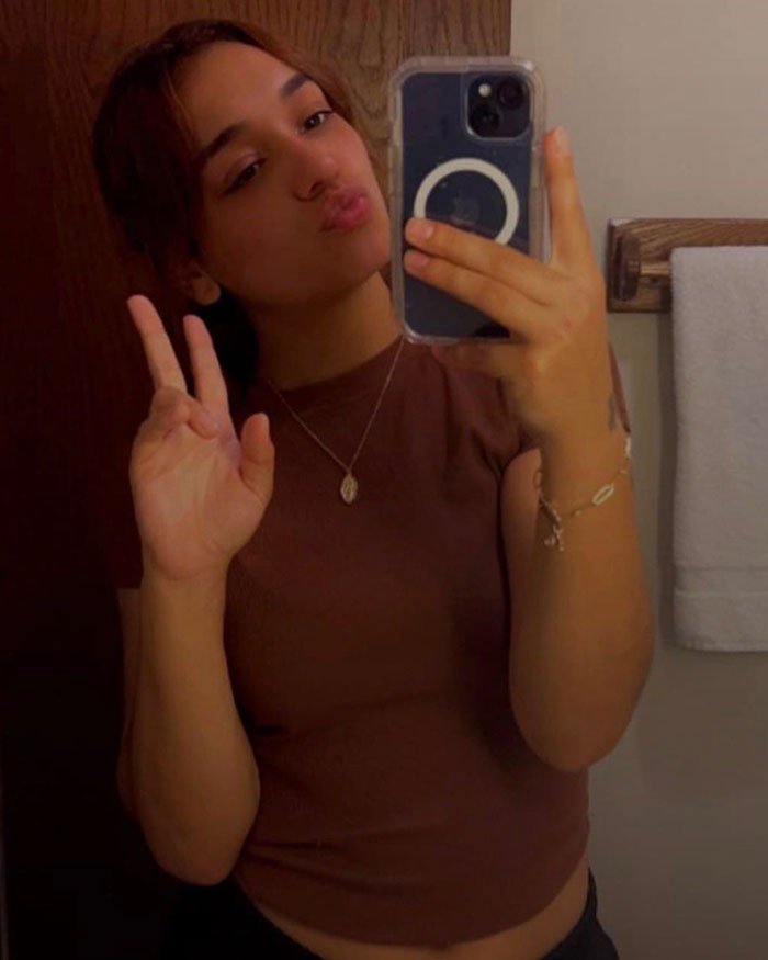 Young woman missing, 24, taking a mirror selfie while making a hand gesture in a casual setting.