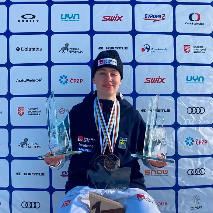 Trans Olympian holding trophies and medals in front of sponsor backdrop amid misgendering incident and debate after NBC footage deletion