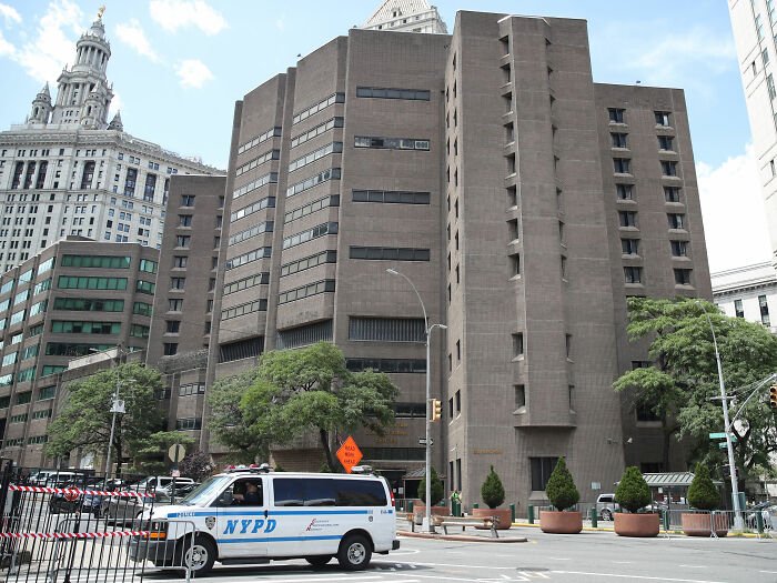 NYPD van outside a large building related to Jeffrey Epstein post mortem investigation in an urban setting.