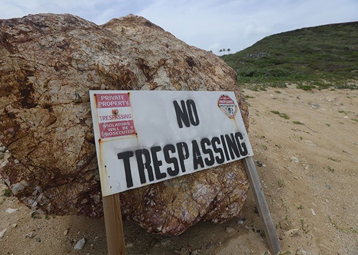 No trespassing sign on rocky terrain with private property warning on a sandy and grassy landscape background.