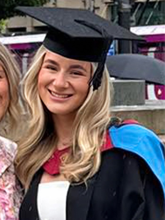 Young woman in graduation cap and gown, smiling outdoors, illustrating legal expert explains dad won't face charges concept.