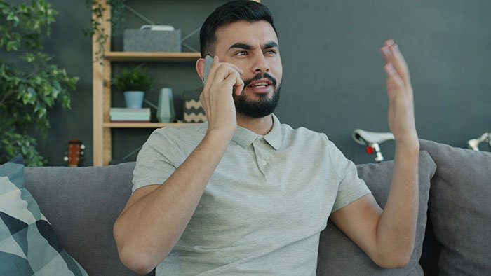 Man with beard talking on phone, appearing frustrated while discussing cheating ex-wife's boyfriend stealing Lego sets.