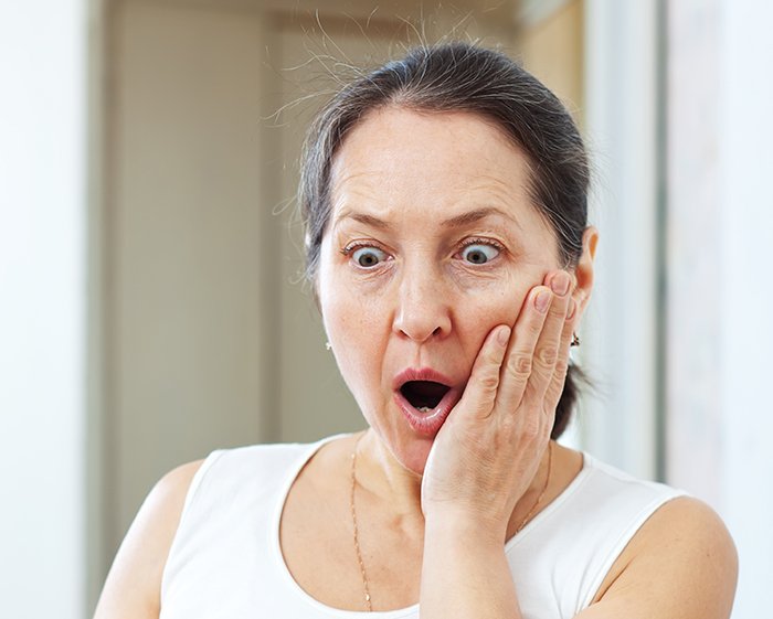 Middle-aged woman with shocked expression, holding face, illustrating in-laws threatening CPS over new parents' home.