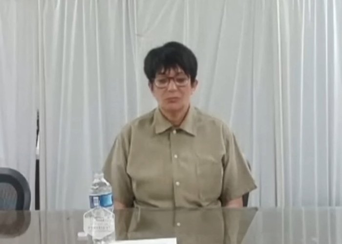 Ghislaine Maxwell wearing glasses and beige shirt seated at table with water bottle in prison appearance amid viral theory discussion