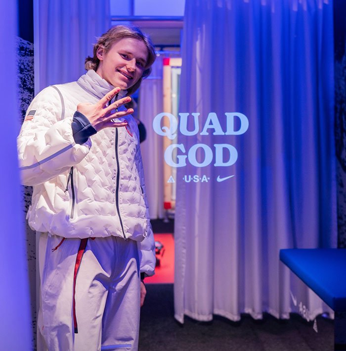 Ilia Malinin posing in a white jacket under blue lighting with quad god text after Olympic performance concerns.