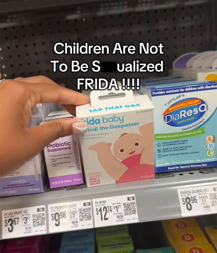 Hand holding Frida Mom gas relief product in store aisle with text about inappropriate marketing controversy.