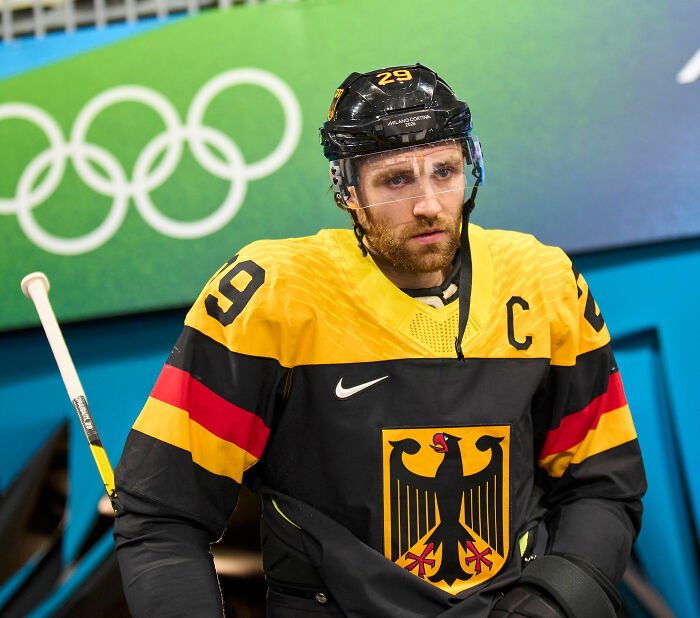 Olympic hockey player in yellow and black uniform with captain patch during intense hot-mic moment between rivals.
