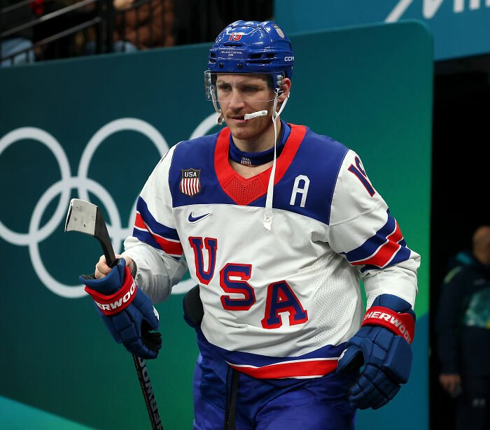 Olympic hockey player wearing USA jersey and helmet during a heated rivalry moment on the ice at the Winter Games.