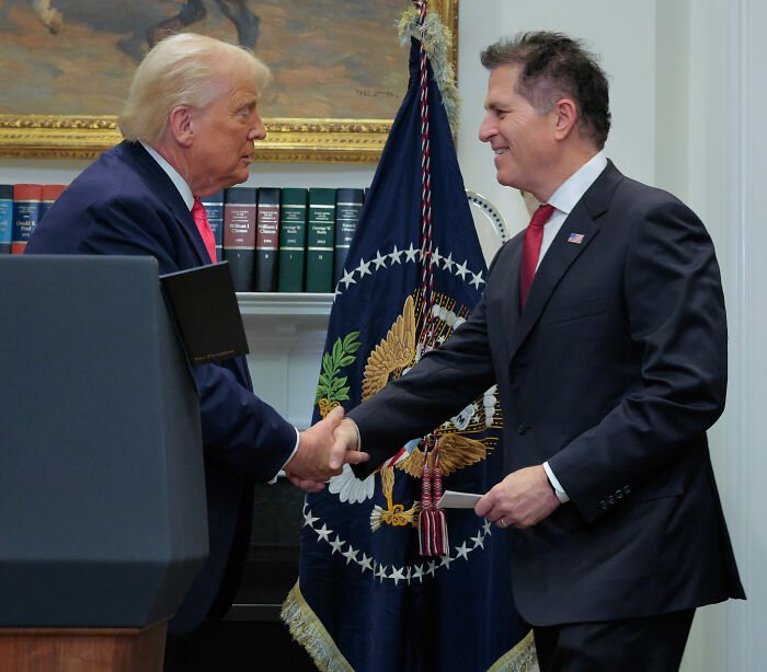 Two men shaking hands during a White House press conference, with a presidential flag in the background.