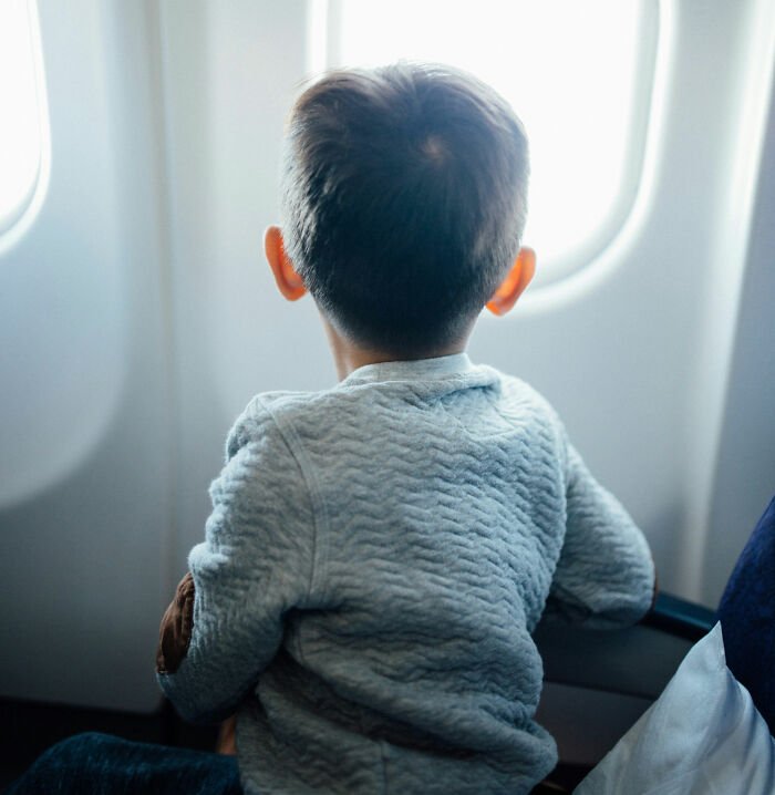 Toddler seated alone on airplane looking out window, highlighting Southwest seating policy controversy.