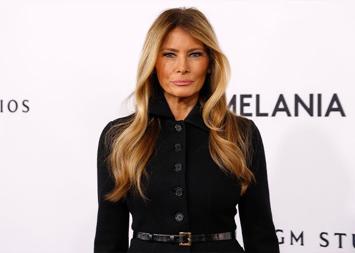 Melania Trump at an event, wearing a black buttoned dress with long wavy hair, highlighting Americans views on First Ladies.