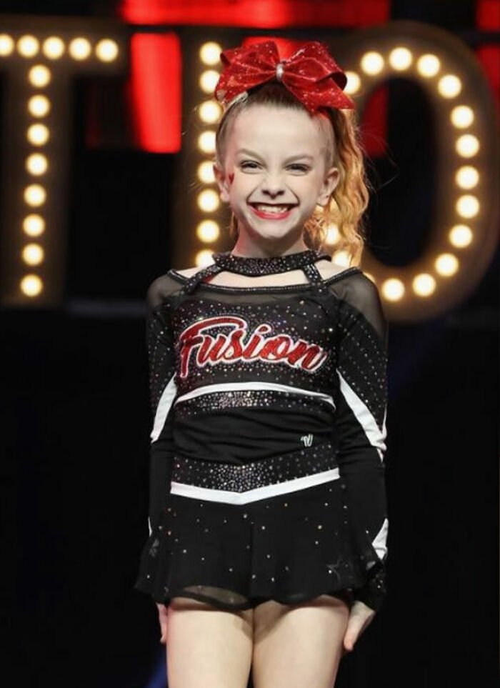 Young cheerleader in a Fusion uniform smiling on stage, related to Utah dance mom’s mean texts and parent clash.