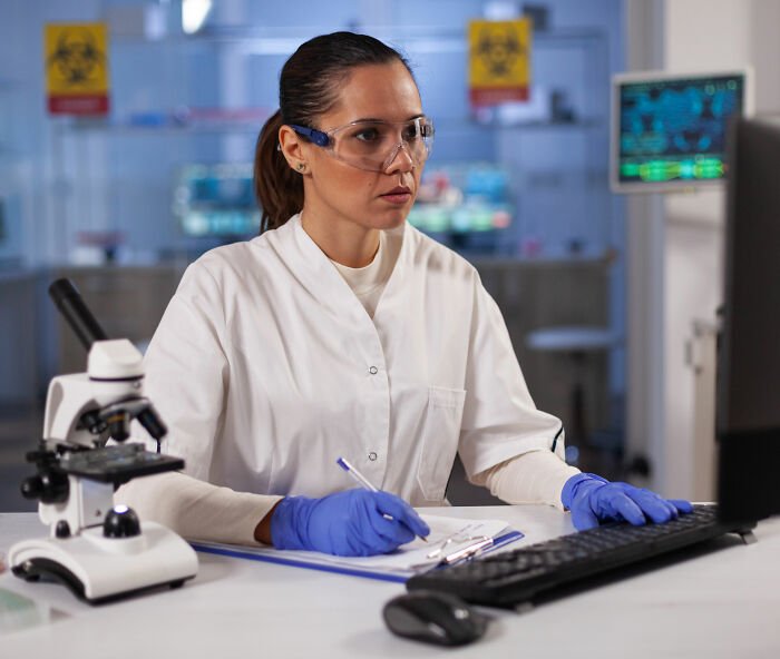 Scientist in lab coat and gloves analyzing data on computer, focused on colon cancer breakthrough research.